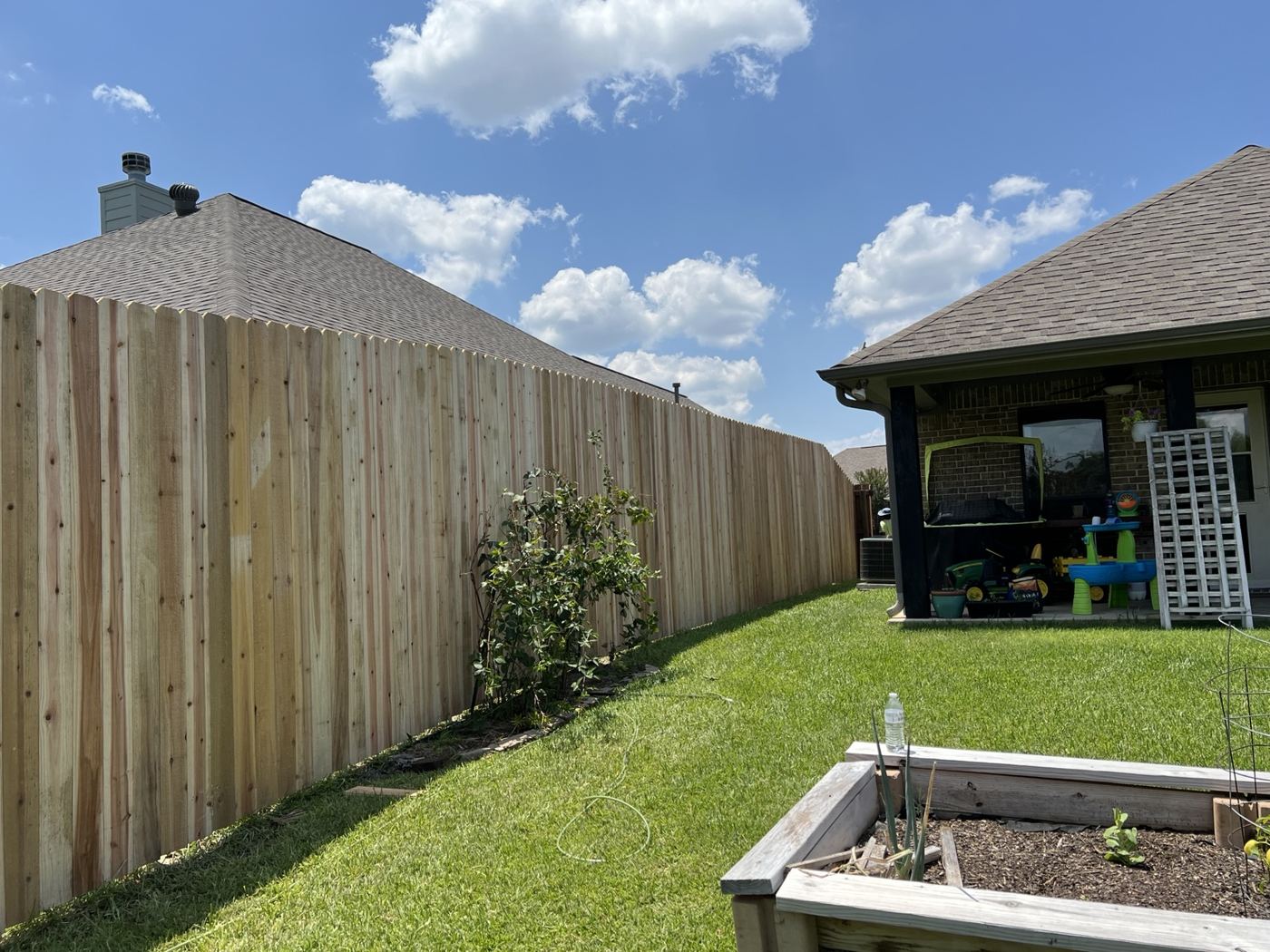 Tall wood privacy fence along a backyard with a covered patio and raised garden beds