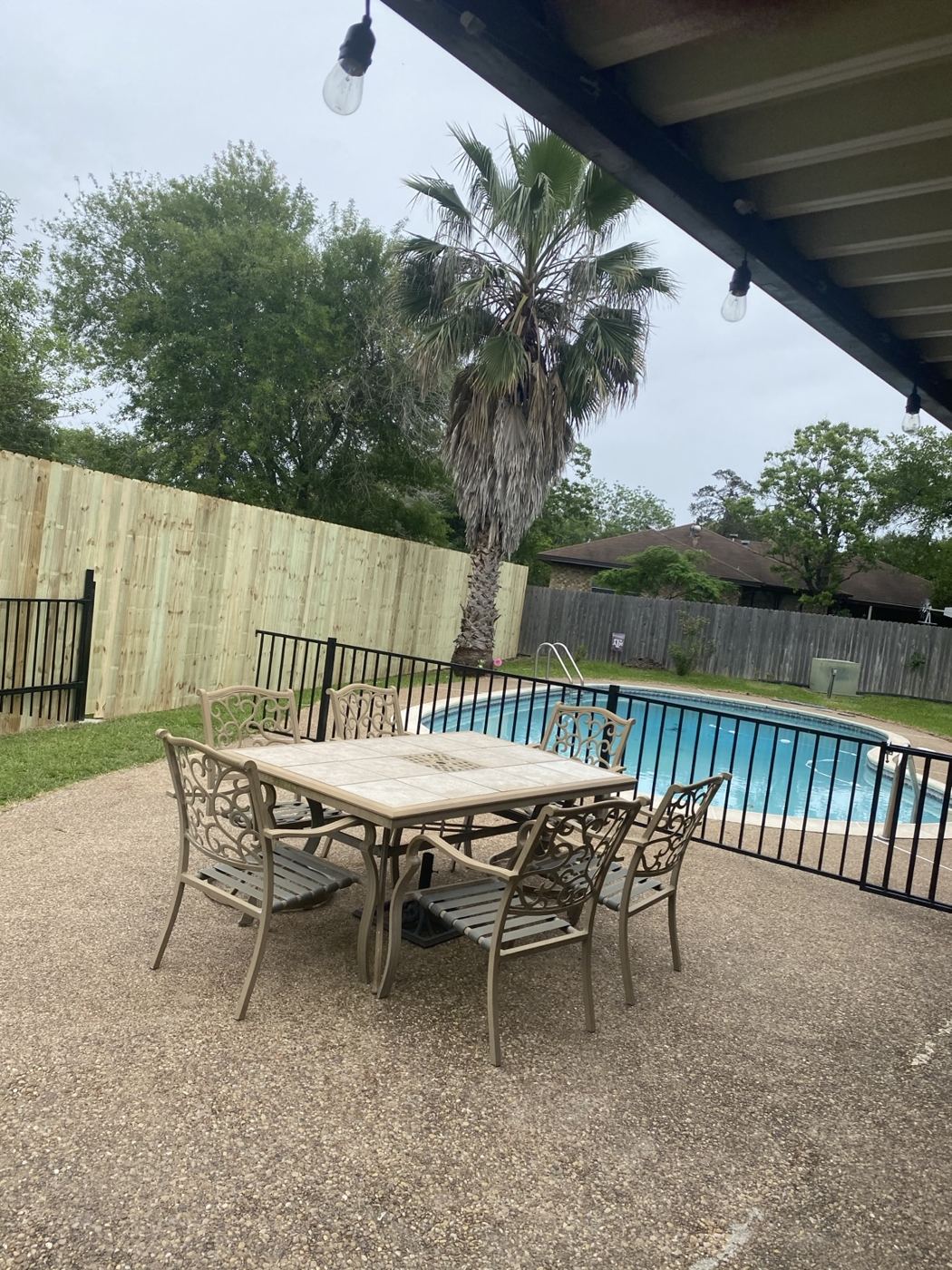 Wood privacy fence and black metal pool fence around a backyard pool and patio