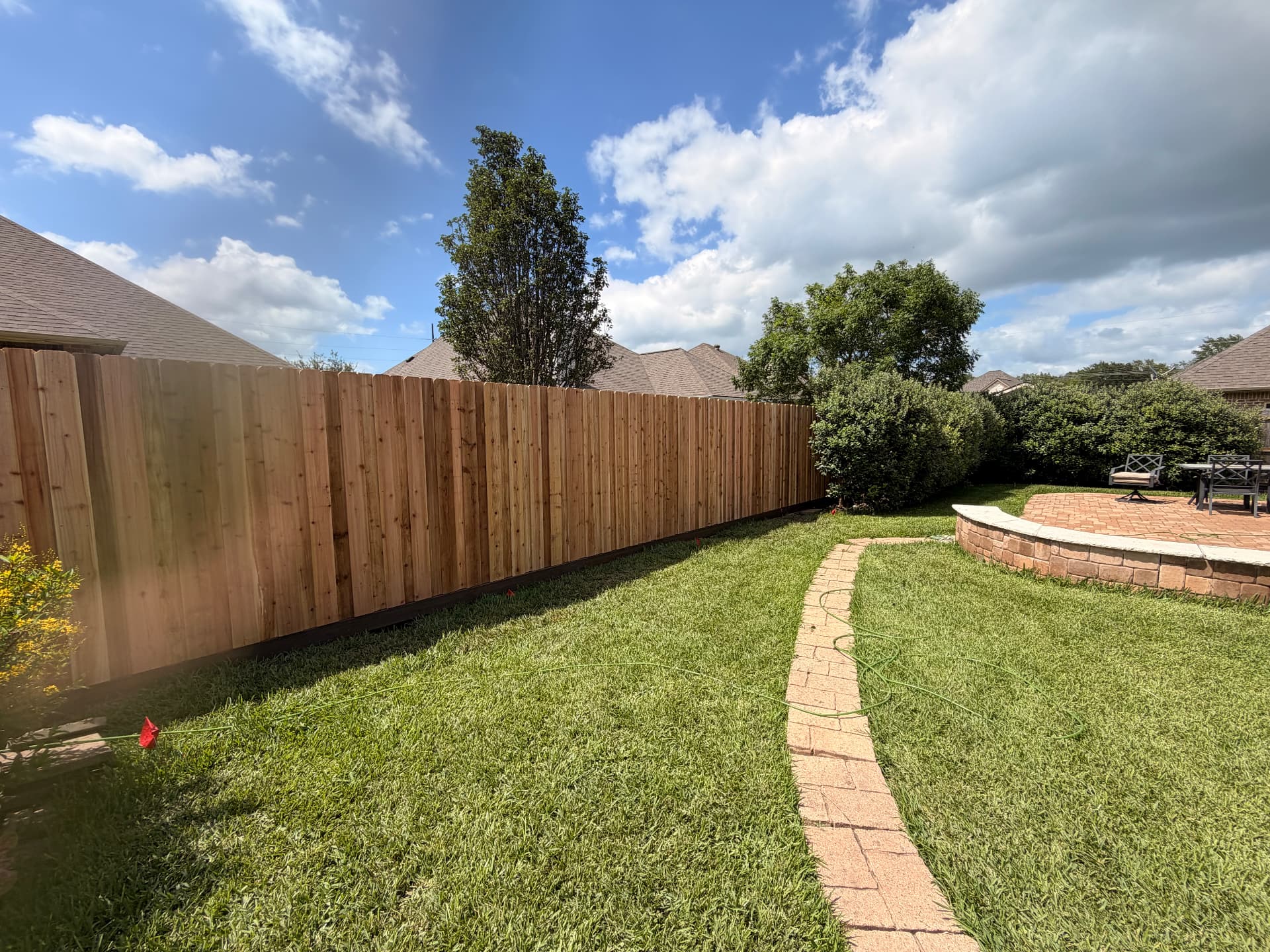 Long cedar privacy fence with a dark rot board running along a Bryan, Texas lawn