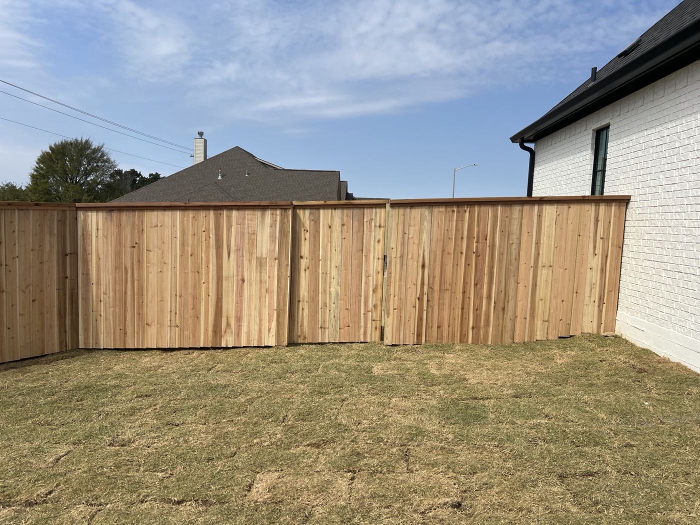 Cedar privacy fence with cap rail beside a white brick home