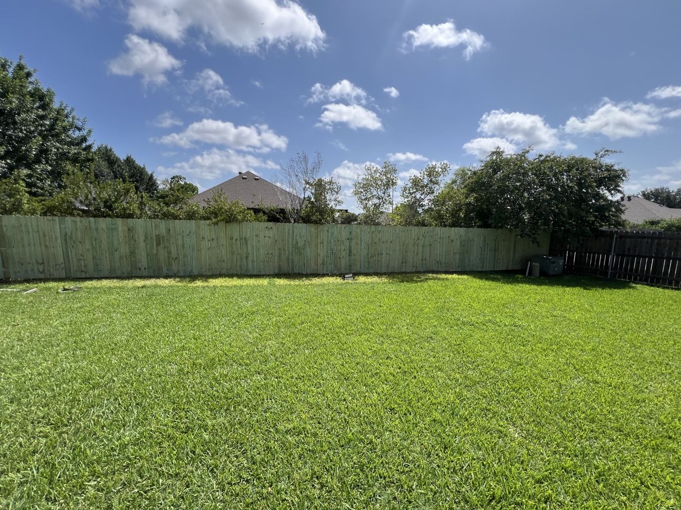 Wood privacy fence enclosing a wide manicured backyard lawn