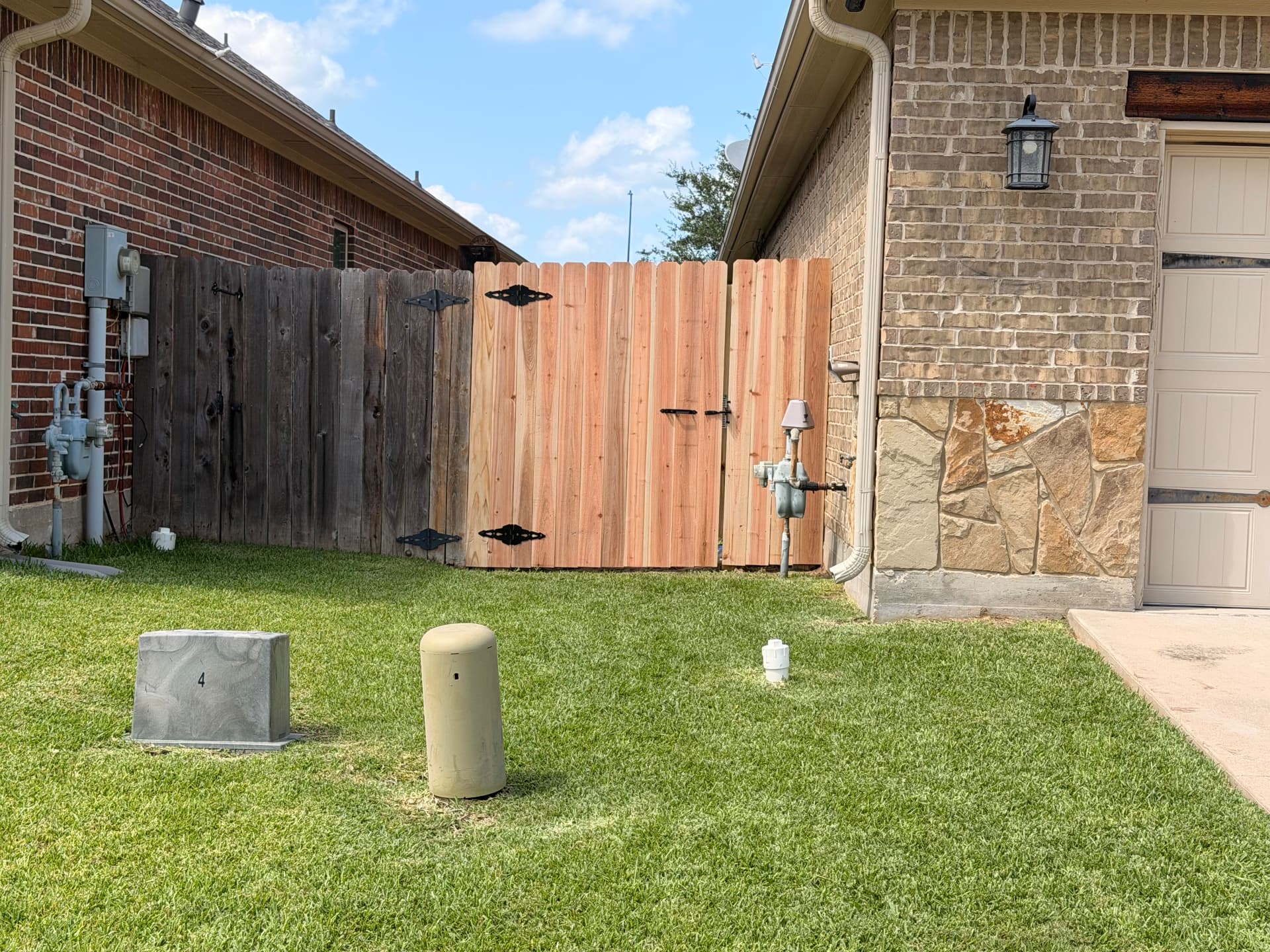 Replacement cedar side-yard gate with black decorative hinges between two brick homes in Bryan TX