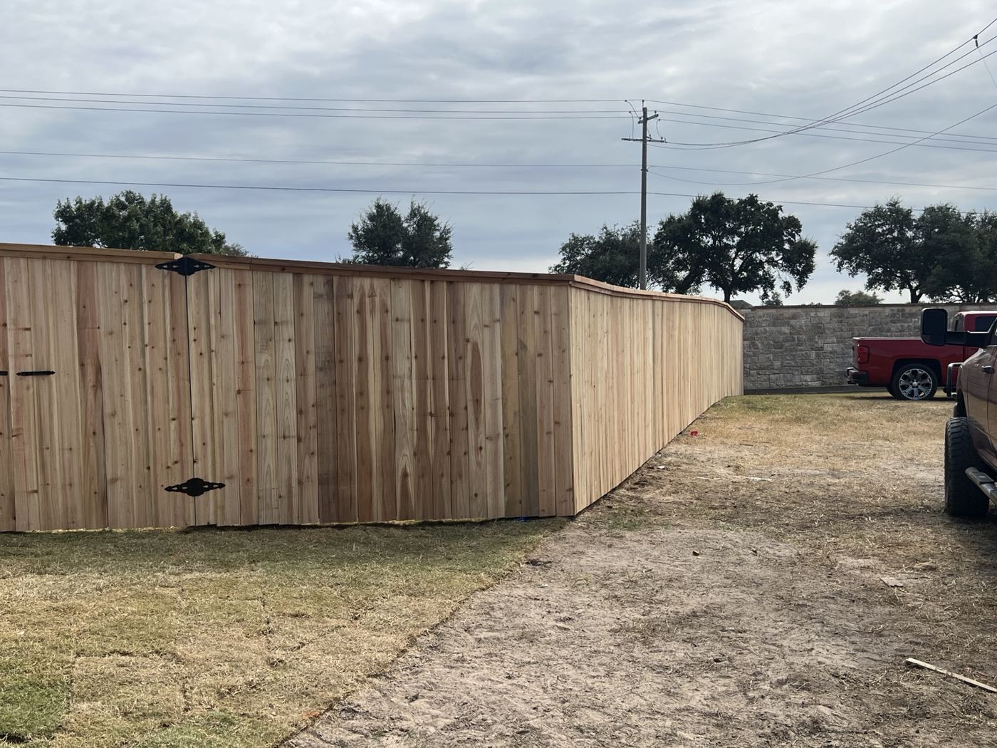Long cedar privacy fence with cap rail running beside a gravel drive