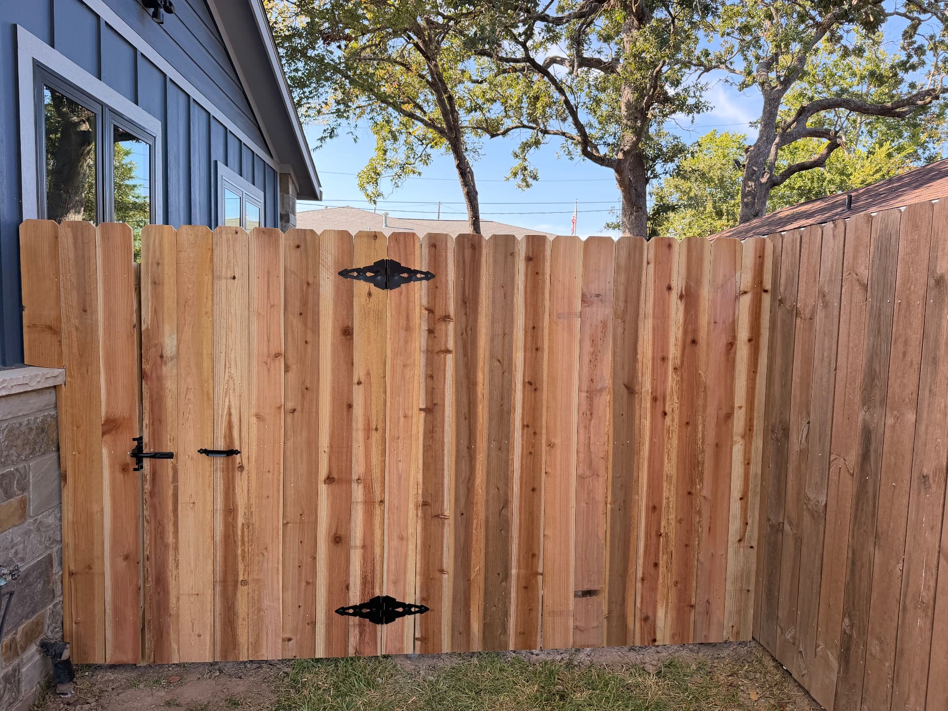 Custom cedar double gate with black strap hinges in a wood privacy fence in Bryan TX