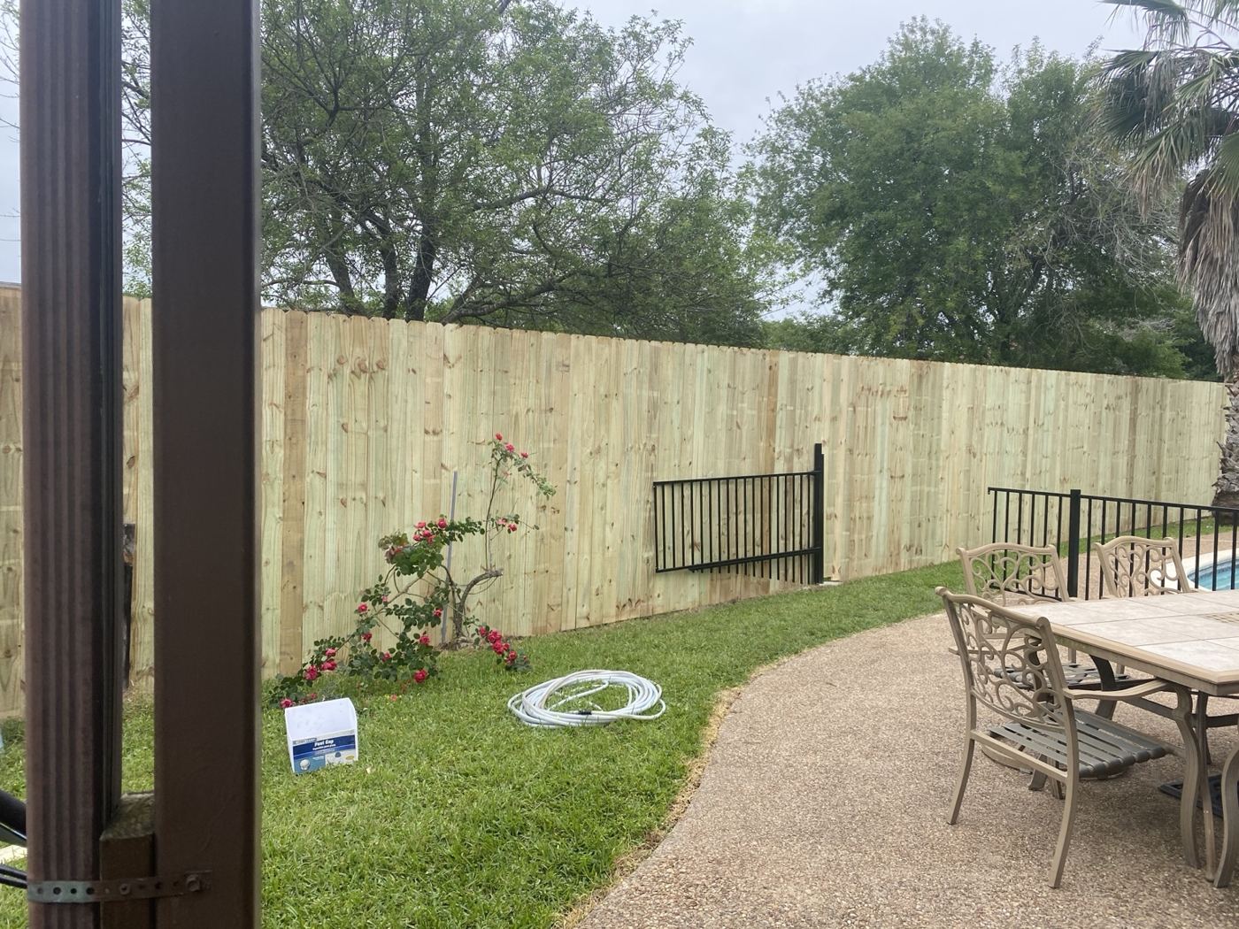 Wood privacy fence behind a pool patio with flower beds
